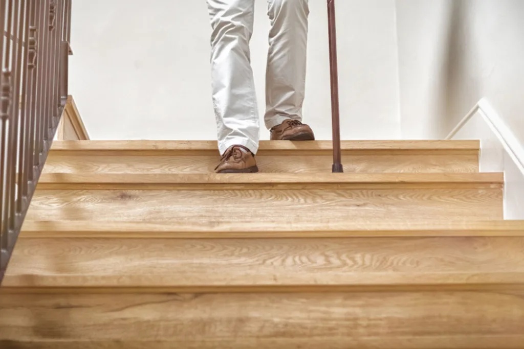 an individual with a walking cane approaches the top of a flight of stairs, ready to descend