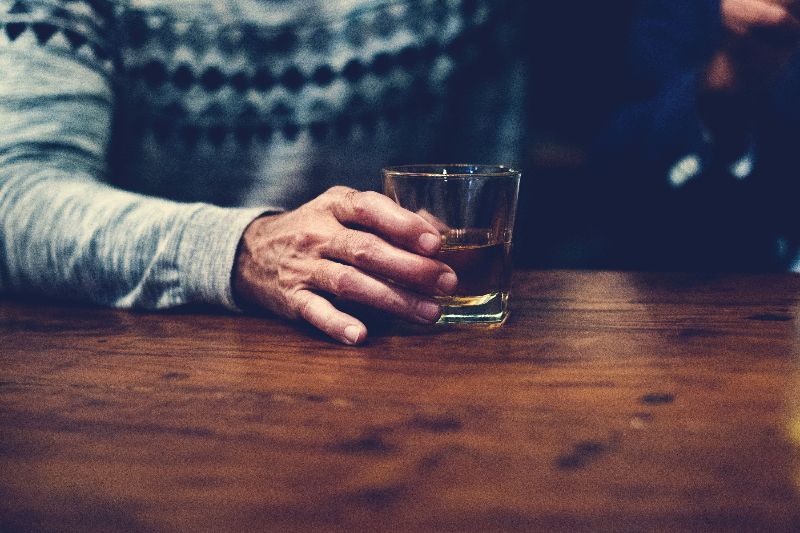 A male hand with a tumbler of alcohol.