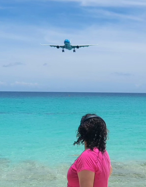 Carmen Cusido watches a plane land on Maho Beach. She is wearing noise-protective headphones.