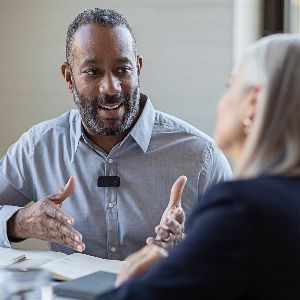 A man wearing a Starkey StarLink mic talks to a woman in a restaurant.