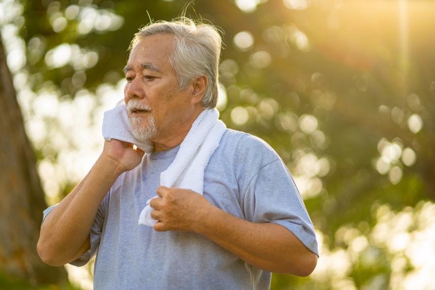Man outside with a towel wrapped around his neck, wiping his face