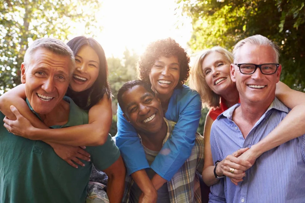 3 sets of elderly heterosexual couples pose for the camera; the women are all being carried piggyback by their husbands