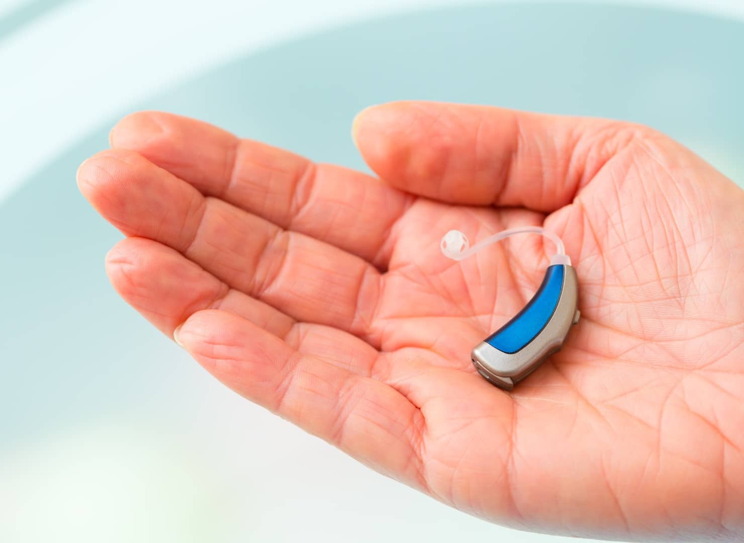 hand hold one gray and blue colored non-prescription hearing aids