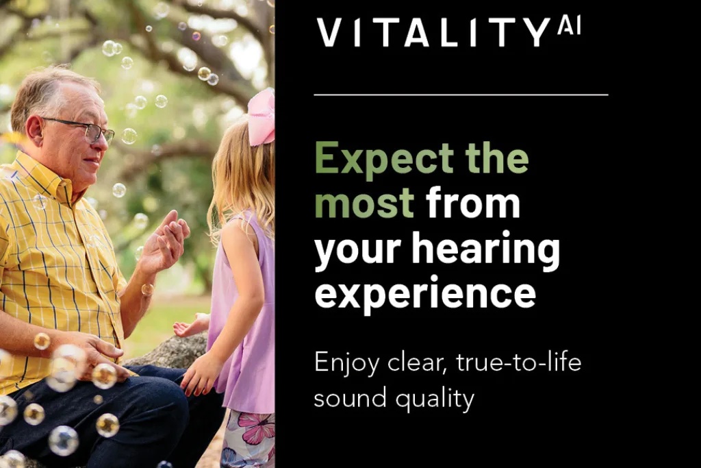 grandfather with hearing aids spends time with granddaughter outside, blowing bubbles and laughing