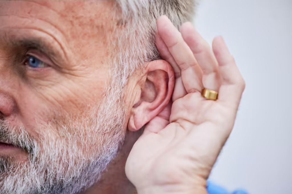 older man cups his hand to his ear as if listening intently for some sound