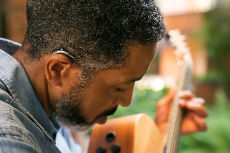 A man wearing a hearing aid plays the guitar.
