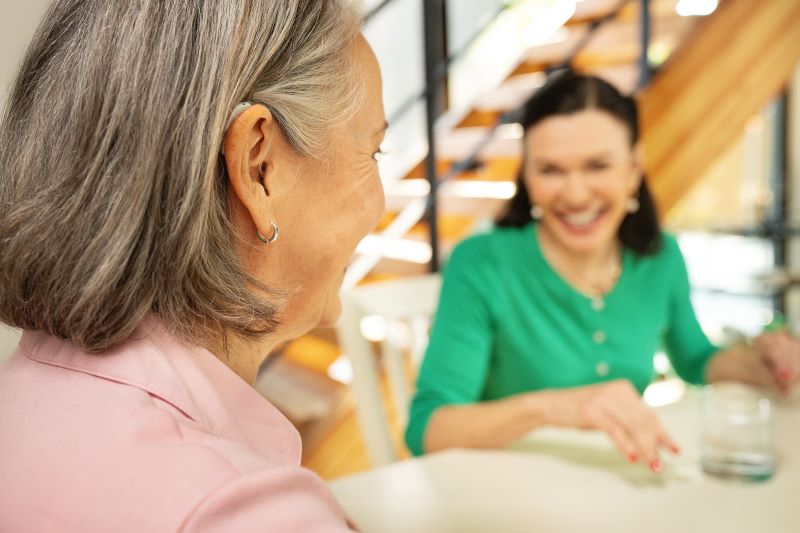 A woman with a hearing aid laughs with her friend.