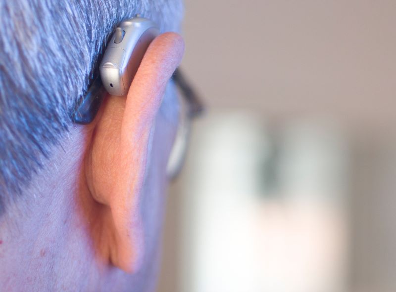 A man wears hearing aids and eyeglasses, seen from behind.